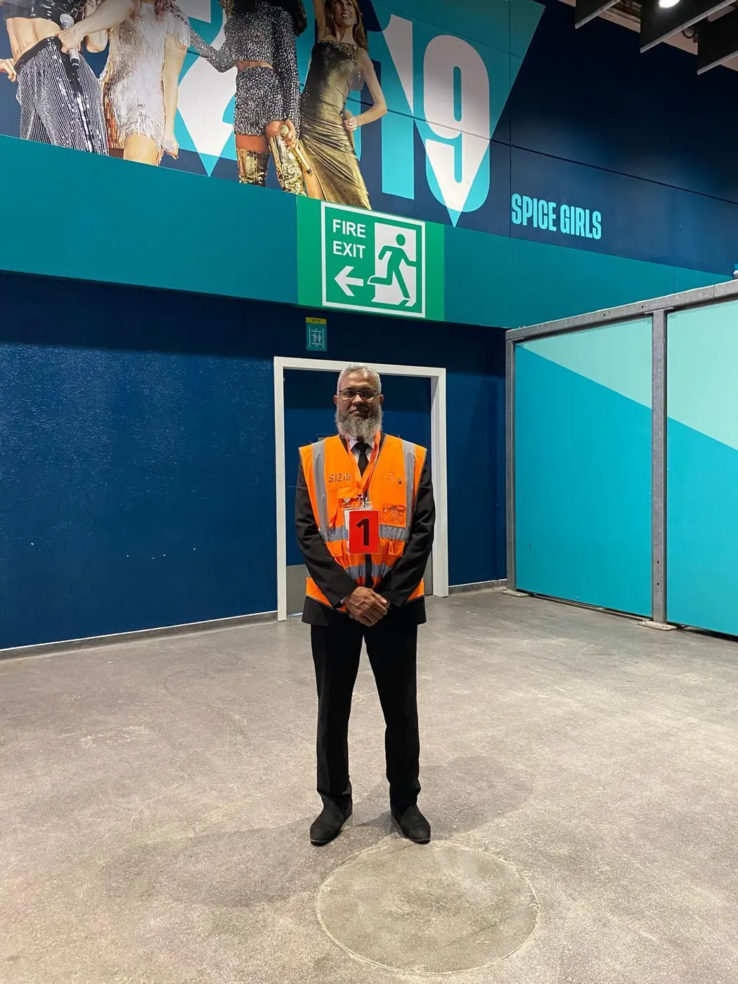 Steward in orange hi-vis standing beside a fire exit inside a venue